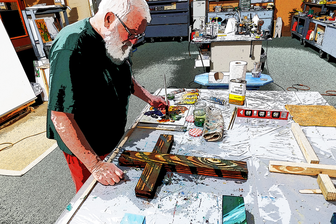 Artisan painting a wooden cross at his workbench in the studio
